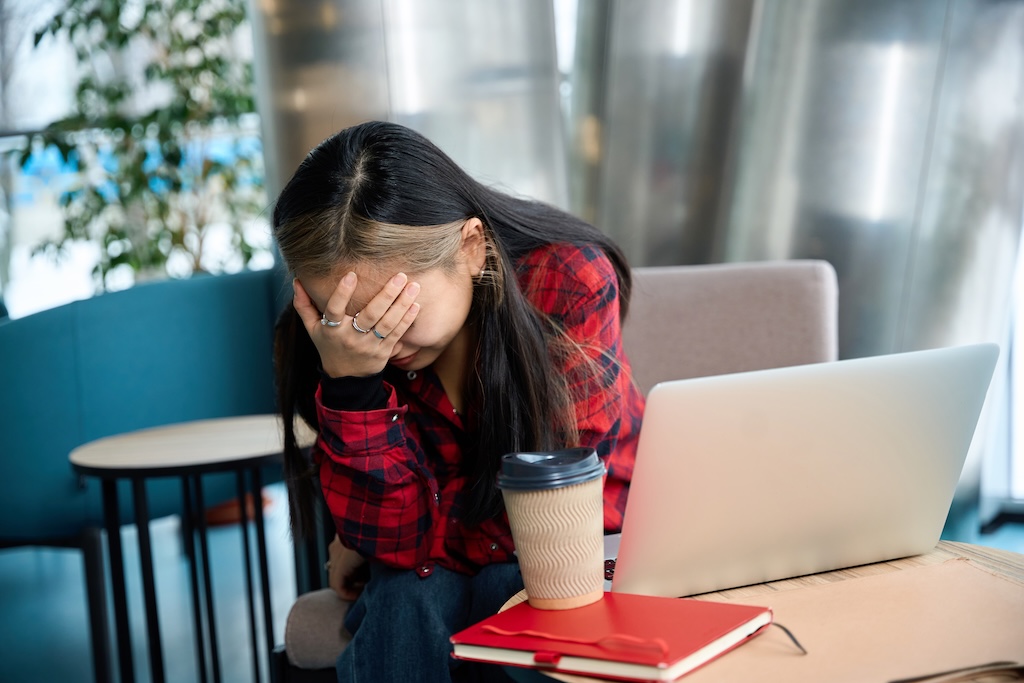 Young tired female with headache touching her head during work at table in coworking office. Struggling with adderall or ADHD medication addiction and misuse.