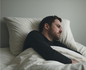 Man lying in bed under the covers, turned away from the camera with a tense, restless expression, illustrating physical and emotional distress commonly associated with delirium tremens.