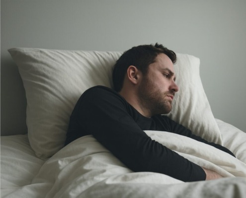 Man lying in bed under the covers, turned away from the camera with a tense, restless expression, illustrating physical and emotional distress commonly associated with delirium tremens.