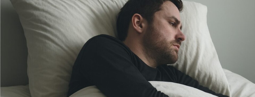 Man lying in bed under the covers, turned away from the camera with a tense, restless expression, illustrating physical and emotional distress commonly associated with delirium tremens.