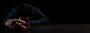 A man with his head down on a table holding a glass of alcohol wondering what are the best detox programs for alcohol.