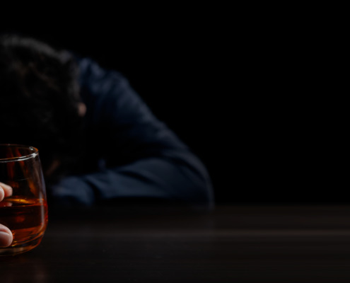 A man with his head down on a table holding a glass of alcohol wondering what are the best detox programs for alcohol.