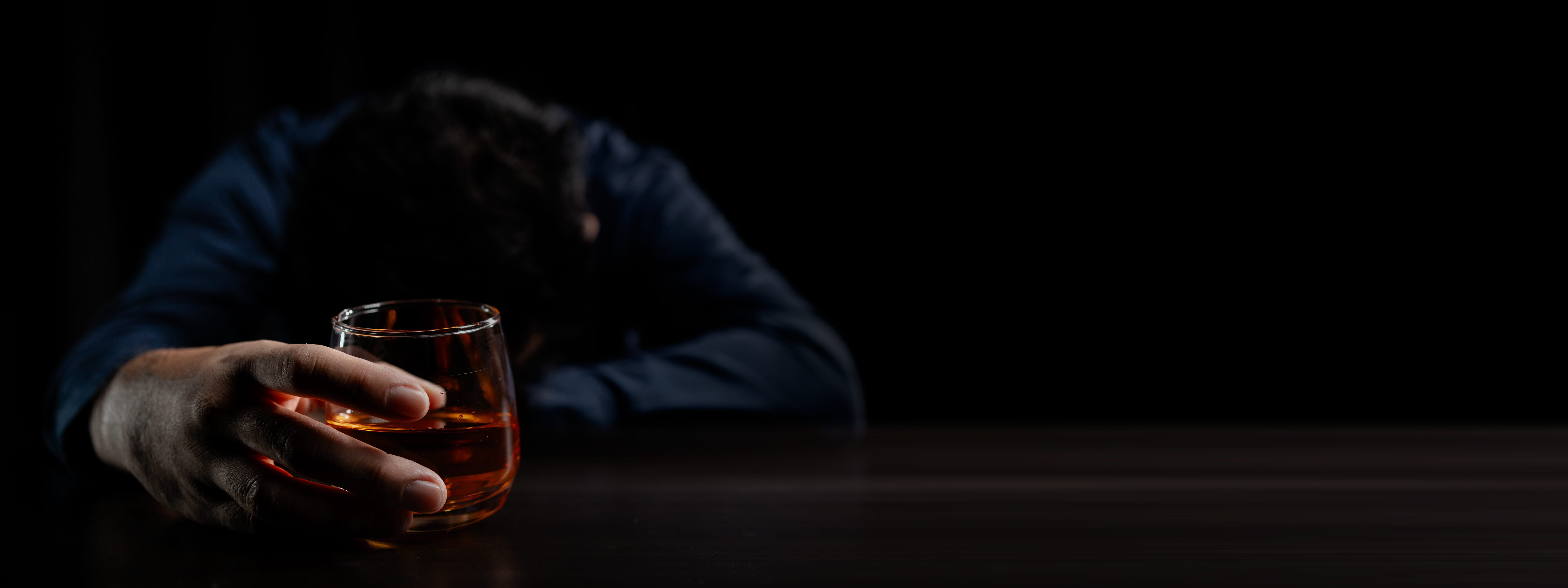 A man with his head down on a table holding a glass of alcohol wondering what are the best detox programs for alcohol.
